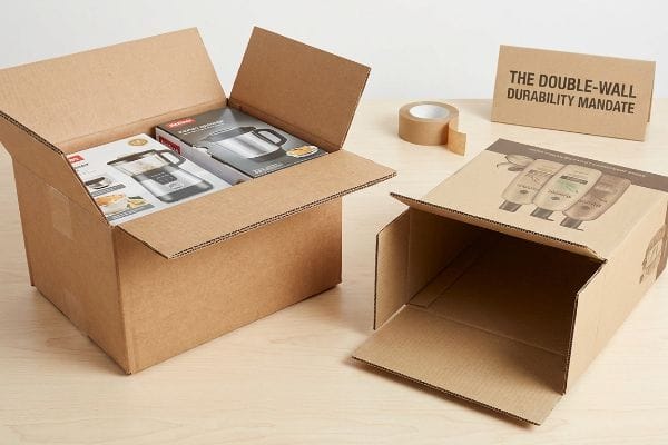 Corrugated cardboard boxes: one with a Rapid Washer and Kettle, another empty with shampoo bottles. The Double-Wall Durability Mandate sign.