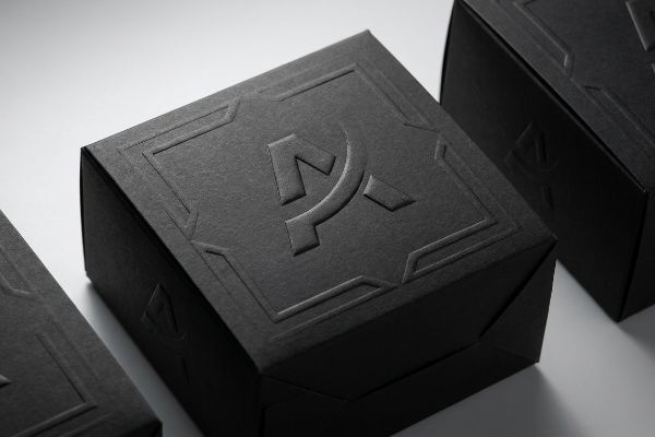 Textured black paperboard box with a raised, three-dimensional embossed geometric logo and border, conveying premium luxury.