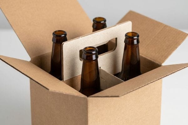 A corrugated cardboard six-pack carrier with four empty amber glass bottles, ideal for sustainable beer packaging.