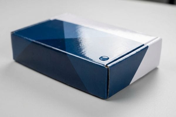 Uma caixa retangular altamente reflexiva exibe um design geométrico em azul escuro e branco, enfatizando sua laminação brilhante.