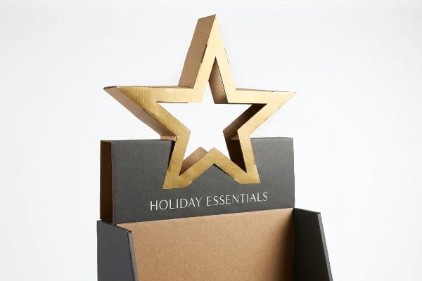 Gold-colored 3D die-cut cardboard star header on a dark grey retail display featuring 'Holiday Essentials' text.