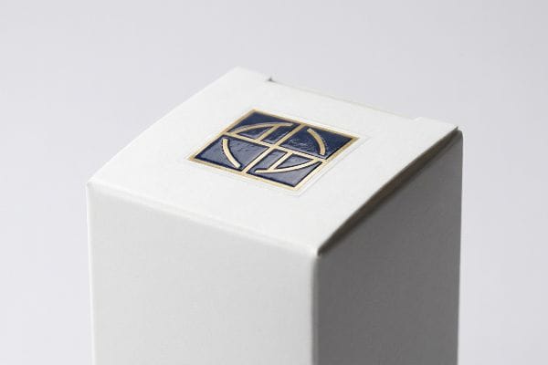 White paperboard packaging box with a dark blue and gold foil geometric logo, showcasing a premium tactile spot gloss finish.