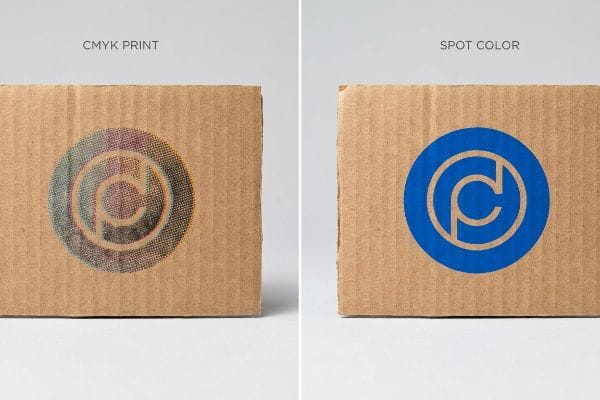 Corrugated cardboard displays two logo prints: a muddy CMYK Print with halftone dots and a sharp, vibrant blue Spot Color logo.