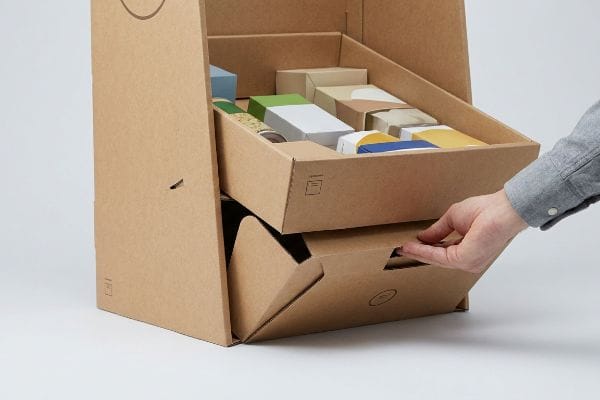 Hand pulling modular tray from natural brown corrugated cardboard retail display, filled with colorful product boxes.