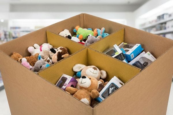 The brown corrugated cardboard dump bin features internal H-dividers, separating sections of plush toys and boxed electronics.