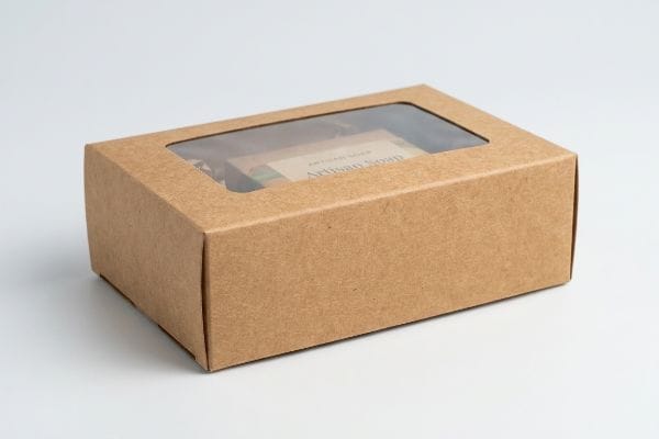 Brown Kraft paper window box showcasing 'Artisan Soap' through its clear top, on a white surface.