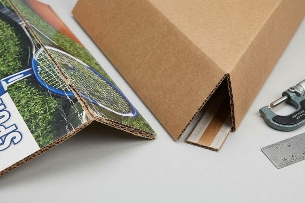 Printed corrugated board with litho-cracking at a 90-degree fold, contrasted with a clean brown board, measured by a micrometer and ruler.