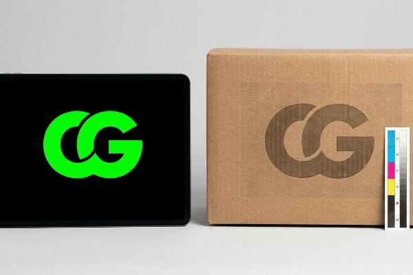 Neon-green CG logo on a digital screen contrasting with a muddy brown CG logo on a corrugated cardboard box, beside a CMYK color calibration strip.