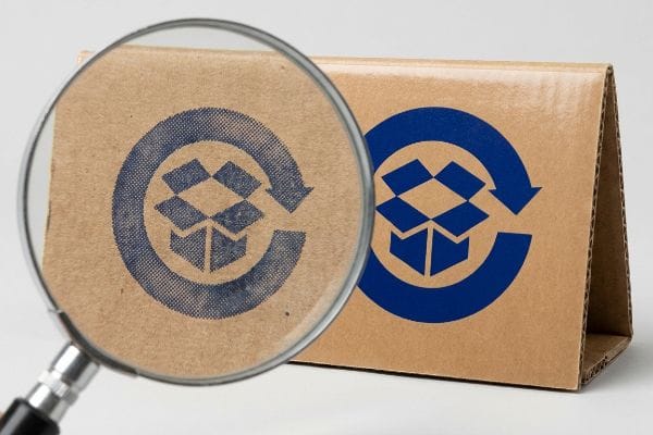 Corrugated board with a blue box-and-arrow logo, magnified to show halftone visual grain versus crisp spot color flood.