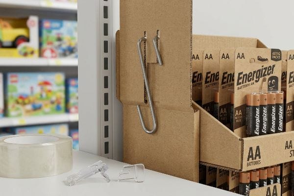 Corrugated cardboard Energizer AA battery sidekick display with a metal S-clip on gondola shelving, next to clear tape and broken plastic clips.