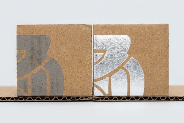 Natural kraft board blocks showcasing dull grey ink versus reflective metallic silver spot color on a corrugated base.