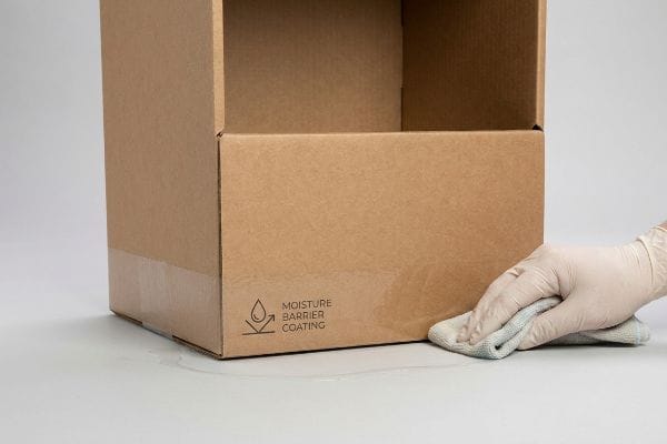 Brown corrugated box featuring a 'Moisture Barrier Coating' symbol, with a gloved hand wiping water from its water-resistant base.