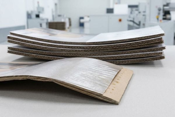 Corrugated cardboard panels with visible fluting and a laminated top sheet display severe moisture warping and bowing from PVA adhesive.
