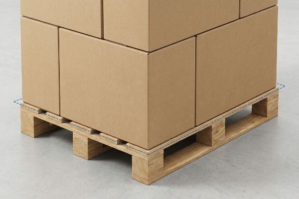 Brown cardboard boxes perfectly aligned on a wooden GMA pallet, illustrating a zero-overhang footprint with dashed lines to prevent transit crush damage.