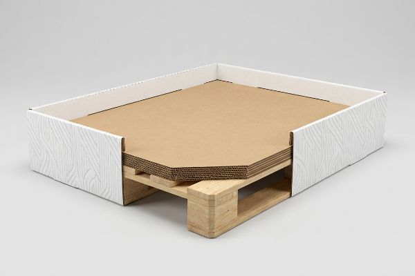 Las láminas de cartón corrugado se apilan sobre un palé de madera clara, revestidas con faldones estructurales blancos de sutil textura ondulada, formando una sólida base de exhibición para puntos de venta.