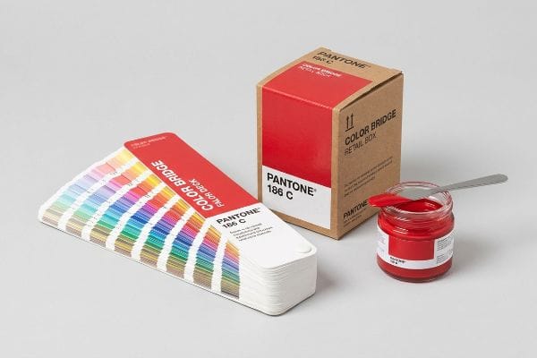 A Pantone Color Bridge fan deck and a Pantone 186 C retail box are displayed with a jar of red ink.