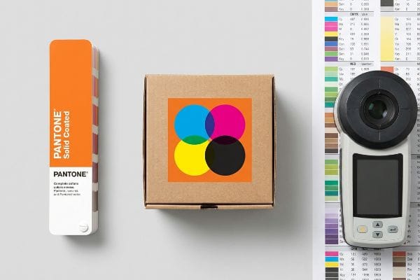 Pantone Solid Coated swatch, CMYK color circles on a cardboard box, and a spectrophotometer for accurate color matching.