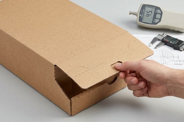 Hand opening SRP box tear-away panel. Force gauge 4.5 lbs, caliper, and drawing detail 0.11 inch cut, 0.05 inch gap.
