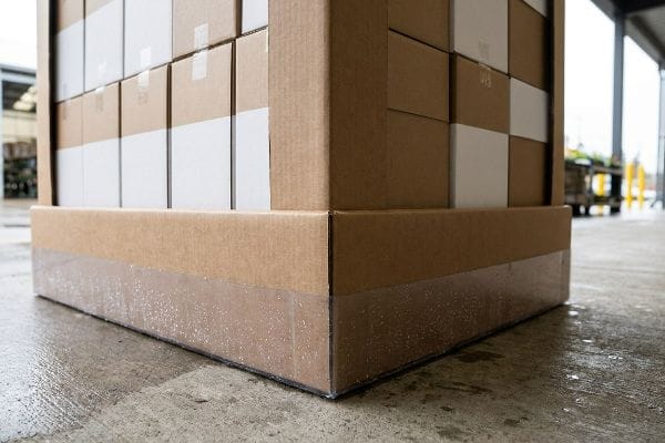 Outdoor pallet display base with clear polymer barrier on wet concrete, preventing moisture wicking from the corrugated board.