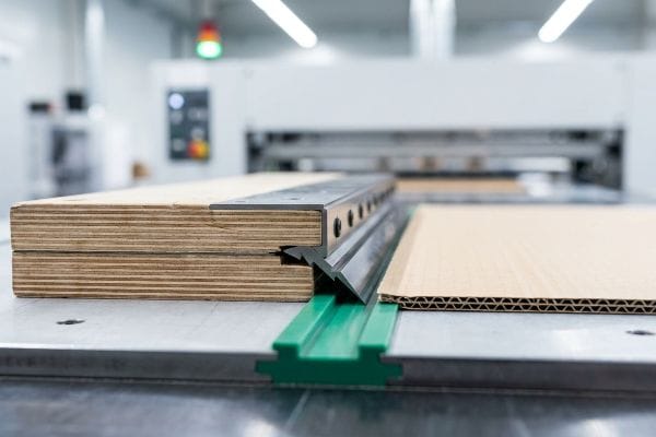 特写镜头展示了瓦楞纸板上的钢制压痕模具,黑色聚合物压痕刀和绿色压痕矩阵通道清晰可见,并显示了瓦楞纸板的瓦楞纹路。.