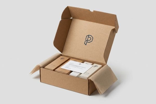 Open brown corrugated PR package with custom-branded products, a welcome card, and a dark P logo on the lid.