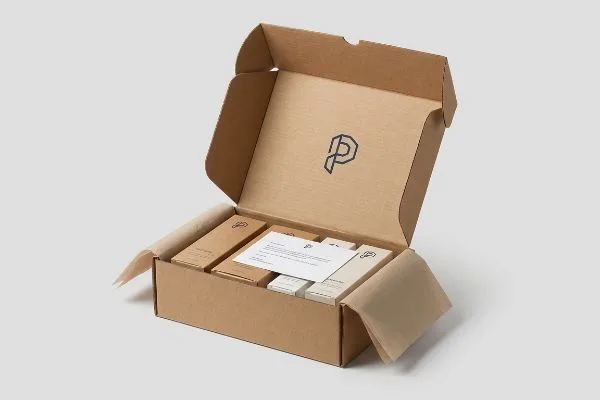 Emballage promotionnel en carton ondulé brun ouvert, contenant des produits personnalisés, une carte de bienvenue et un logo P foncé sur le couvercle.