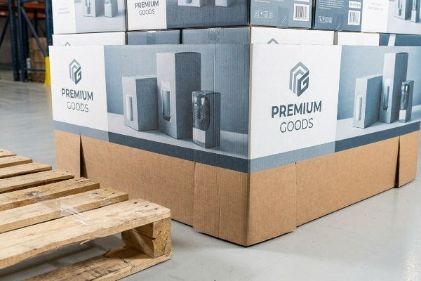 Printed corrugated pallet skirt for 'Premium Goods' retail display, concealing the industrial base of a bulk merchandising unit next to a wooden shipping pallet.