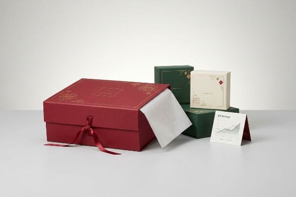 Elegant holiday packaging featuring a red gift box with gold foil and satin ribbon, alongside smaller green and cream boxes and a Q4 Strategy card.
