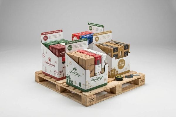 Wooden GMA pallet supports holiday quarter-pallet displays featuring festive graphics, filled with products, next to a measuring tape and caliper for precise retail merchandising.