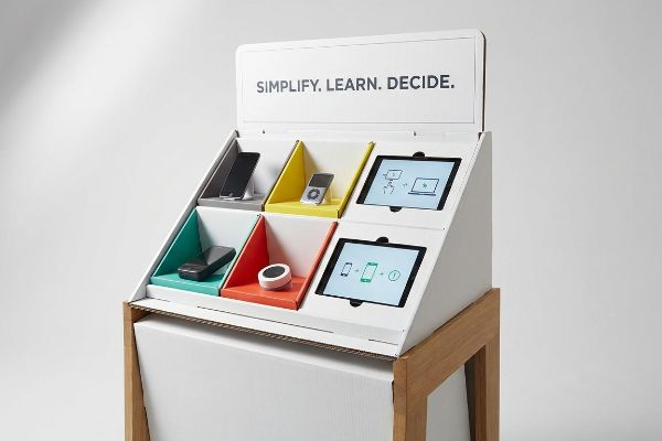 Educational POP display with electronics in colored compartments. Tablets show diagrams. Header: 'Simplify. Learn. Decide.'