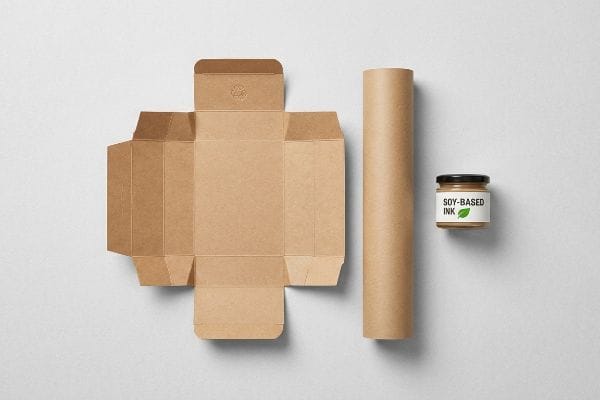 Displaying eco-friendly packaging components, an unfolded brown cardboard box with a recycling symbol, a kraft paper tube, and a jar of Soy-Based Ink.