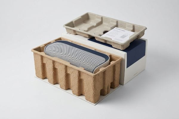 Brown molded pulp tray holding a blue speaker with a grey fabric top, next to a retail box and instruction manual.