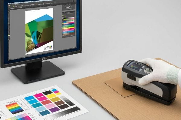 Espectrofotómetro para medir el color del cartón ondulado, junto a un monitor Dell con el software GMG y una prueba CMYK.