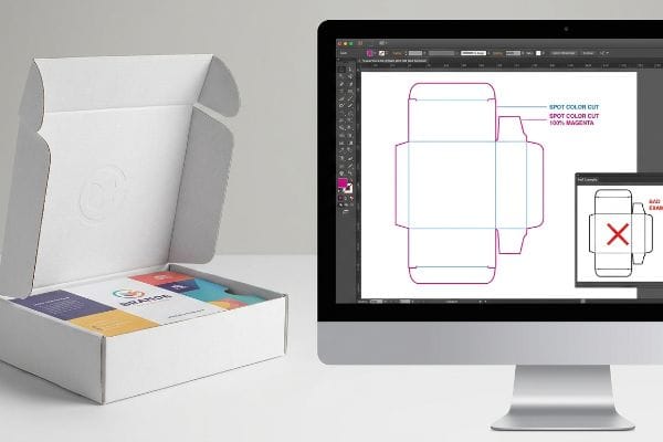 White mailer box with 'Brandol' inserts and a computer screen showing a vector dieline with Spot Color Cut (100% Magenta) lines.