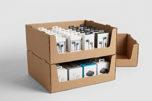 Two stacked brown cardboard PDQ trays display white and black earbud product boxes, ready for retail.