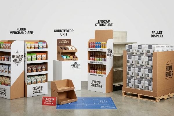 Corrugated cardboard retail displays: a Floor Merchandiser with Organic Snacks, a Countertop Unit for Premium Chocolates, an Endcap Structure for New Arrivals Beverages, and a Home Goods Pallet Display. A sign notes 'Ada Compliant (E-Flute)' and 'Structural Failure (Scaled Pre-Line)'.