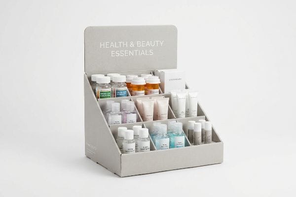 Showcasing Health & Beauty Essentials, a tiered grey cardboard display holds small bottles, tubes, and lip balms.