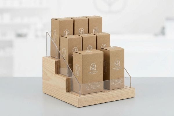A tiered wooden and clear acrylic retail display stand showcases nine Earth Road Naturals kraft paper boxes, enhancing in-store product merchandising.
