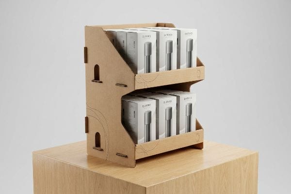 This two-tiered corrugated cardboard retail display, featuring wavy cut-outs, presents Elivio product boxes on a light wood pedestal.