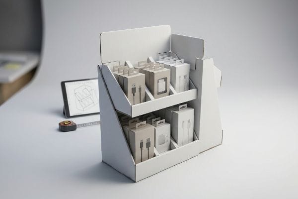 White two-tier custom display box with product boxes, a tablet showing a blueprint, and a measuring tape.