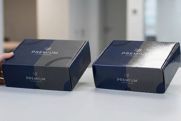 Dark blue and gray custom-printed boxes, featuring 'Premium Custom Printed' text, illustrate glossy UV coating and matte finishes.