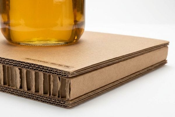 Amber liquid in a glass jar resting on a Double Wall Spine corrugated board, showcasing its virgin kraft flutes and robust honeycomb structure.