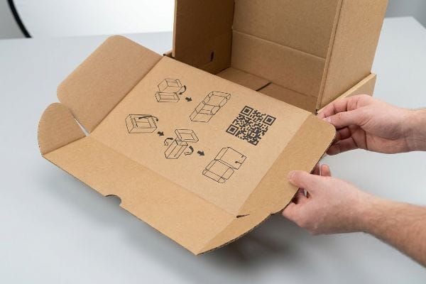 段ボール箱に、文字のない組み立て説明書、線画の図、および内側のフラップに印刷されたQRコードが付属しています。.