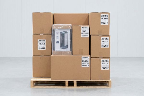 Brown cardboard boxes, labeled 'Walmart Pallet #1 Fragile', stacked on a wooden pallet, one revealing a black appliance.