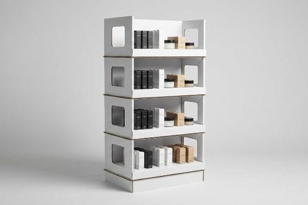 Expositor de cartón corrugado blanco de cuatro niveles, con ventanas laterales estructurales y revestimiento interior blanco, que exhibe cosméticos de alta gama en envases negros, blancos y de papel kraft.