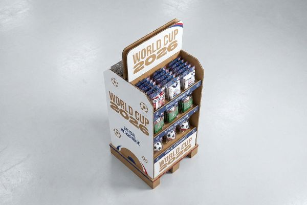A multi-tiered corrugated cardboard display showcases World Cup 2026 Official Merchandise, featuring small soccer balls and packaged items.