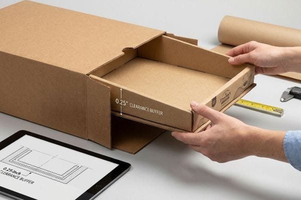 Corrugated master carton with a nested tray being pulled out, clearly showing the 0.25-inch Clearance Buffer, with a design diagram on a tablet.