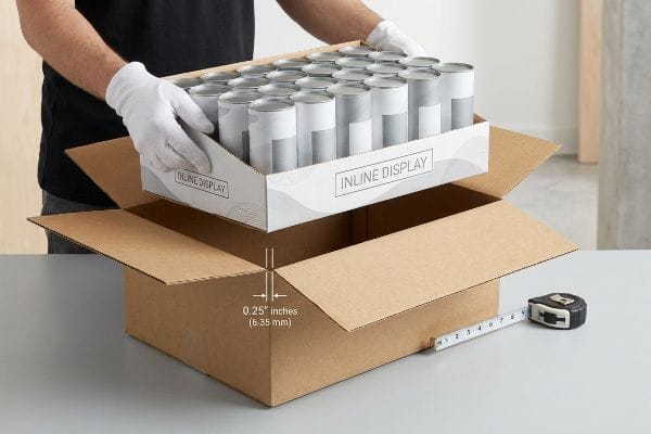 A gloved hand shows the 0.25 inches (6.35 mm) offset for an Inline Display tray in a corrugated shipping box.