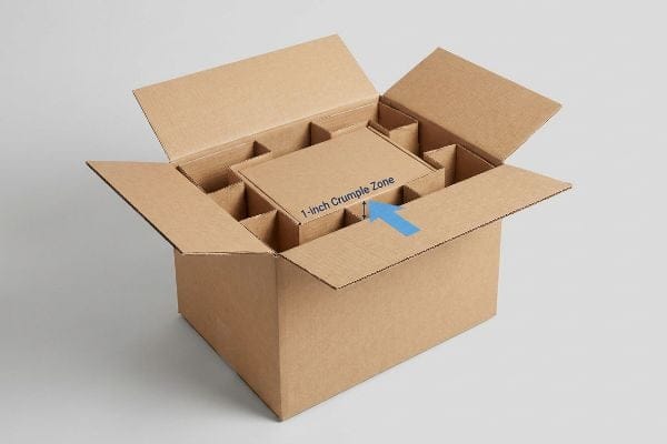 Brown corrugated master carton with internal dividers highlighting a 1-inch crumple zone for product protection.