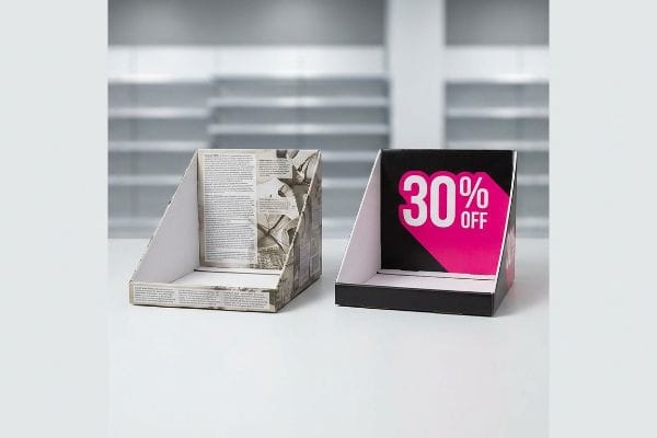 Cardboard PDQ display trays, one with newspaper print, another black with a bold pink '30% Off' graphic, for impulse buying.